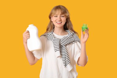 Sarı arka planda elinde şişe ve plastik kapaklı çamaşır deterjanı tutan genç bir kadın.