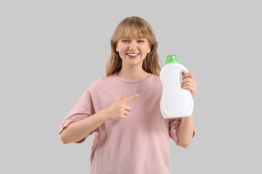 Gri arka planda çamaşır deterjanı şişesini gösteren genç bir kadın.