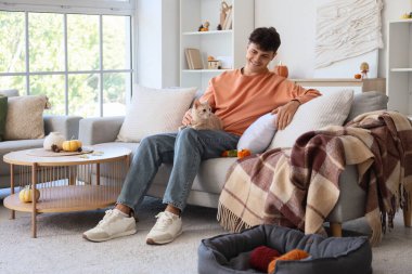 Güz günü evde oturan sevimli kedileri ve balkabakları olan genç adam.