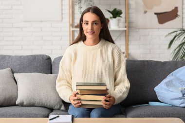 Kitaplar ve defterlerle dolu güzel bir kız öğrenci evdeki kanepede oturuyor.