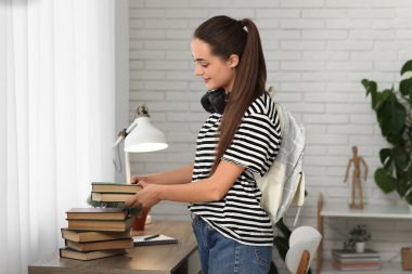 Evde kitap, çanta ve kulaklık yığını olan güzel, mutlu bir bayan öğrenci.