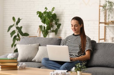Evdeki kanepede dizüstü bilgisayarı olan güzel bir kadın yazar.