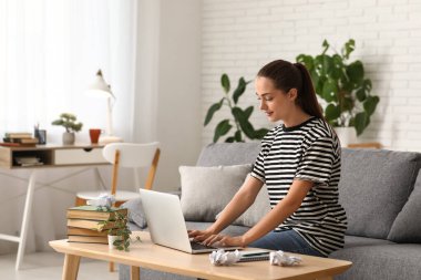 Evdeki kanepede oturan dizüstü bilgisayarı ve kitapları olan güzel, mutlu bir kadın yazar.