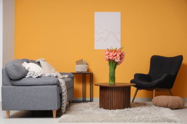 Oturma odasının içinde kanepe, koltuk ve vazoda gladyatör çiçekleri var.