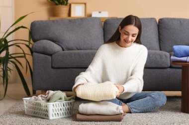 Evde yerde oturan sıcak süveter yığınıyla genç bir kadın.