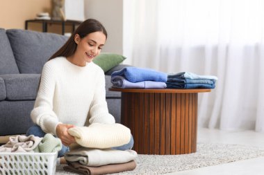 Evde yerde oturan sıcak süveter yığınıyla genç bir kadın.