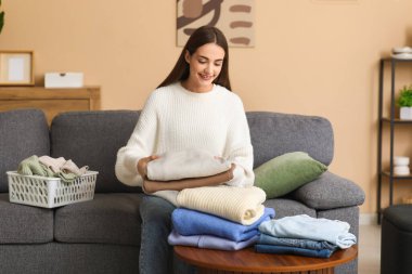 Evde katlanmış giysileri masaya koyan genç bir kadın.