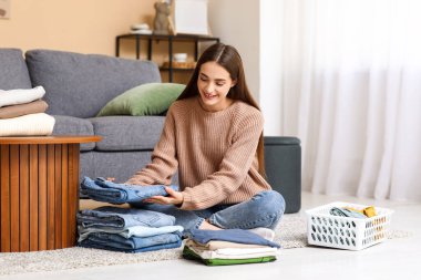 Genç bir kadın evde kot pantolon katlıyor.