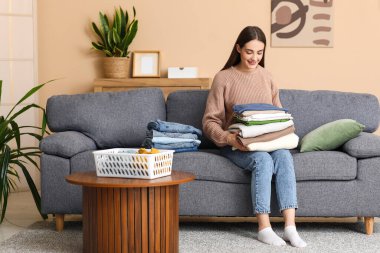 Evdeki kanepede oturan bir yığın elbisesi olan genç kadın.