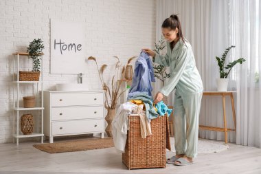 Çamaşır odasında kirli çamaşırlarla dolu sepeti tutan güzel genç bir kadın.