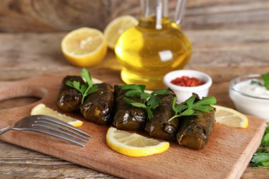Lezzetli Dolmas (doldurulmuş üzüm yaprakları), limon, ekşi krema ve ahşap zemin üzerindeki baharatlarla kesme tahtası