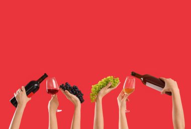 Kırmızı arka planda üzüm, şişe ve şarap tutan kadın eller.