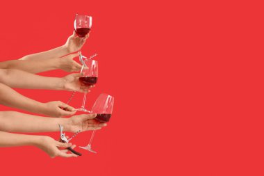 Kırmızı arka planda şarap bardakları ve tirbuşon tutan kadın eller.