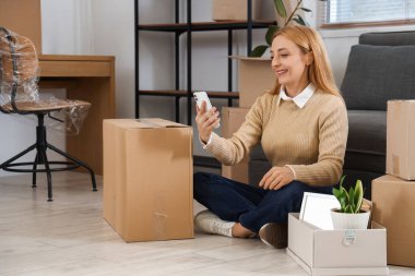 Taşındığı gün ofisinde cep telefonu kullanan kutuları olan olgun bir iş kadını.