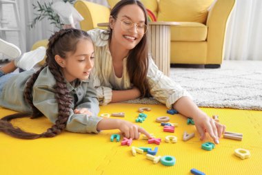 Female speech therapist and little girl with letters lying in office clipart