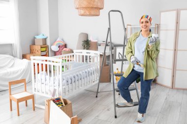 Çocuk odasında boya kutusu ve fırçayla gezen hamile bir kadın.