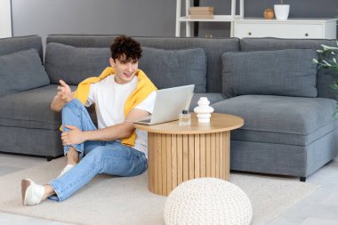 Genç adam evde dizüstü bilgisayarla görüntülü sohbet ediyor.