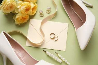 Zarflı alyanslar, kadın ayakkabıları, çiçekler ve yeşil arka planda mücevherler.