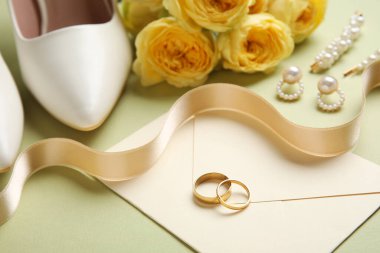 Zarflı alyanslar, kadın ayakkabıları, çiçekler ve yeşil arka planda mücevherler.