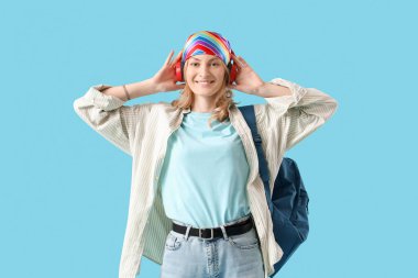 Mavi arka planda sırt çantalı kulaklıklı bayan öğrenci.