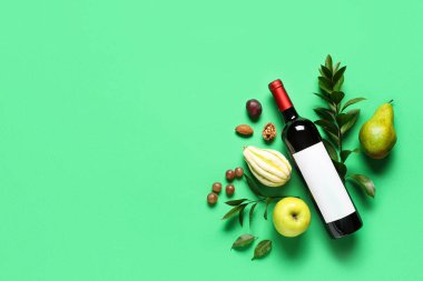 Yeşil zemin üzerinde meyve, yaprak ve balkabağı olan bir şişe şarap.