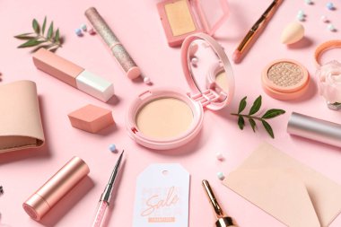 Farklı dekoratif kozmetik ürünleri, aksesuarlar ve pembe arka planda satış etiketine sahip kompozisyon