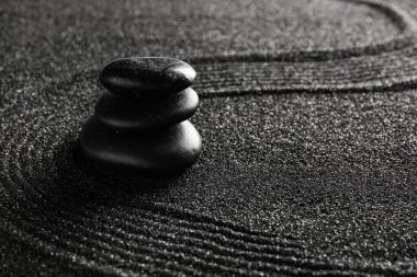 Çizgileri olan siyah kumlar üzerinde taş yığını. Zen kavramı
