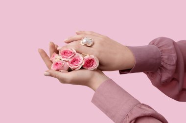 Pembe arka planda güzel gülleri olan zarif bir ringde kadın elleri.