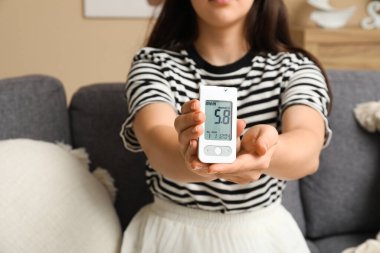 Glukometresi olan şeker hastası genç bir kadın evdeki kanepede oturuyor.