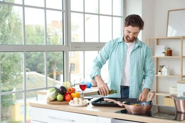 Yakışıklı sakallı adam mutfağa kabak dilimleriyle zeytinyağı döküyor.