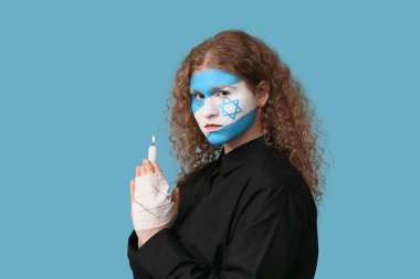 Yüzünde İsrail bayrağı olan genç bir kadın ve yanan bir mum mavi arka plan için dua ediyor. Uluslararası Soykırım Anma Günü