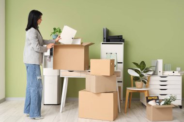 Genç iş kadını, taşınma günü içinde eşyalar olan karton kutulara çerçeveyi yerleştiriyor.