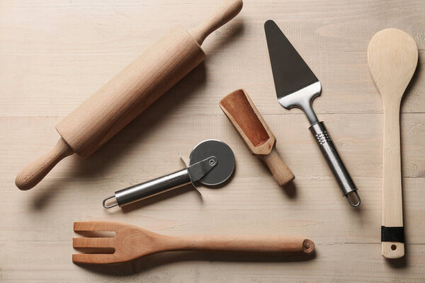 Набор различных кухонных принадлежностей с ножом для пиццы из нержавеющей стали на деревянном фоне