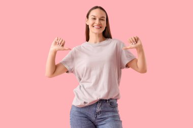 Pembe arka plandaki gri tişörtü gösteren genç bir kadın.