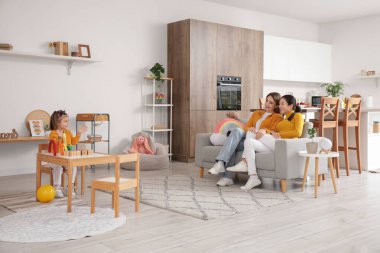 Küçük kızları evde oynarken genç lezbiyen çift kanepede oturuyor.