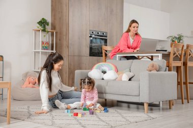 Karısı ve küçük kızı evde oynarken genç lezbiyen kadın dizüstü bilgisayar kullanıyor.