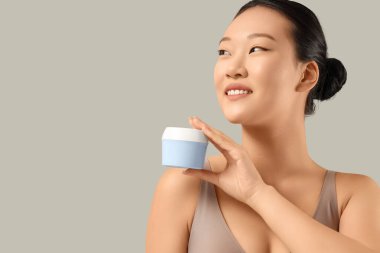 Gri arka planda krema kavanozu olan genç Asyalı kadın, yakın plan.