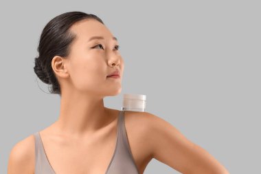 Gri arka planda krema kavanozu olan genç Asyalı kadın, yakın plan.