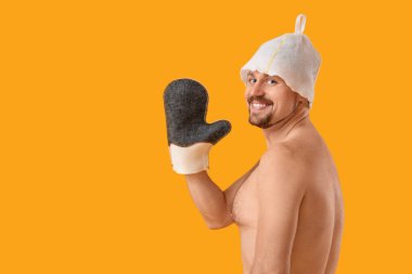 Handsome man in sauna felt hat with massage glove on yellow background clipart