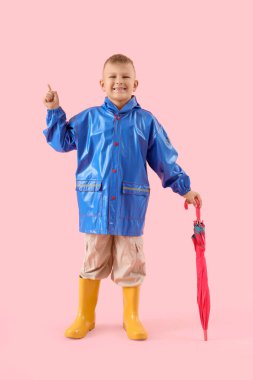 Şemsiyeli şirin küçük çocuk pembe arka plandaki bir şeyi işaret ediyor.