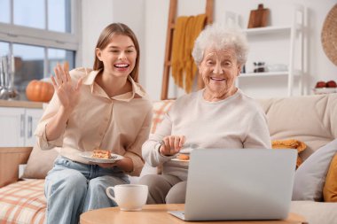 Genç bir kadın ve büyükannesi ellerinde pasta parçalarıyla evdeki kanepede sohbet ediyorlar.