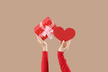 Elinde bej arka planda kalbi olan bir hediye kutusu tutan kadın. Sevgililer Günü kutlaması
