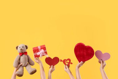 Oyuncak ayılı kadın eller, hediye kutuları ve sarı arka planda kalpler. Sevgililer Günü kutlaması
