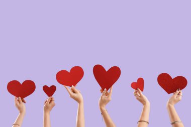 Leylak arkaplanda kırmızı kalpli bir kadın eli. Sevgililer Günü kutlaması