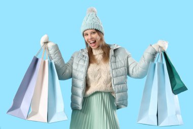 Mavi arka planda alışveriş torbaları olan kışlık elbiseli genç bir kadın.