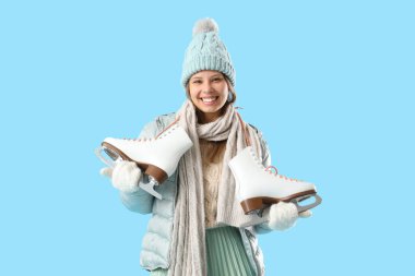 Mavi arka planda buz patenleriyle kışın giyinmiş genç bir kadın.