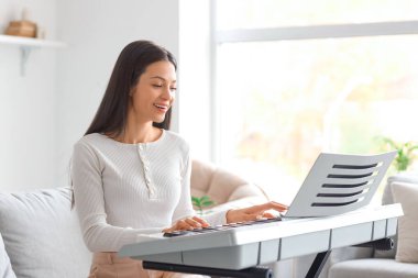 Evdeki kanepede sentezleyici oynayan genç bir kadın.