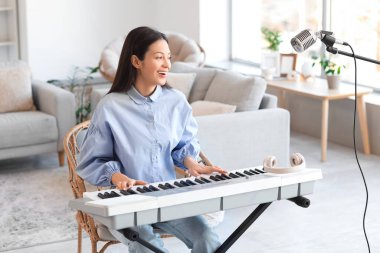 Gülümseyen genç kadın evde sentezleyici çalıyor.