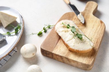 Lezzetli işlenmiş peynirli bir dilim ekmek, mikro yeşil ve ışık masasında mantar.