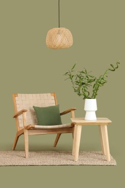 Vazoda bambu saplı masa, yeşil arka planda koltuk ve lamba.